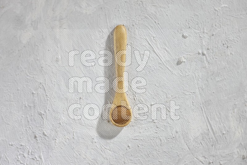 Cinnamon powder in a wooden spoon on a white background