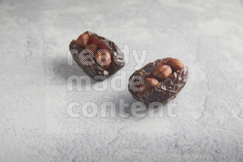 two hazelnuts stuffed madjoul dates on a light grey background