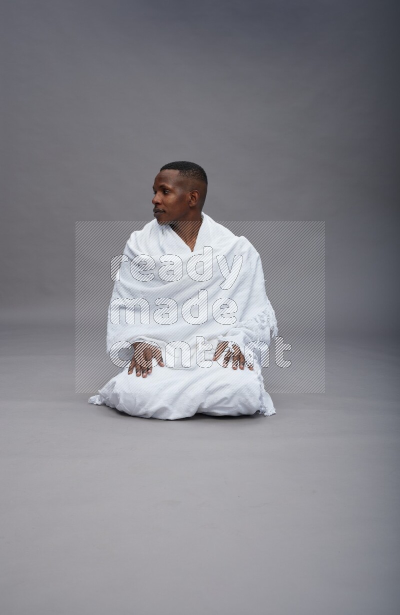 A man wearing Ehram sitting on floor praying on gray background