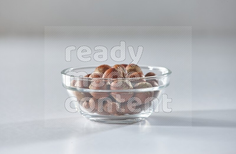 A glass bowl full of hazelnuts on a white background in different angles
