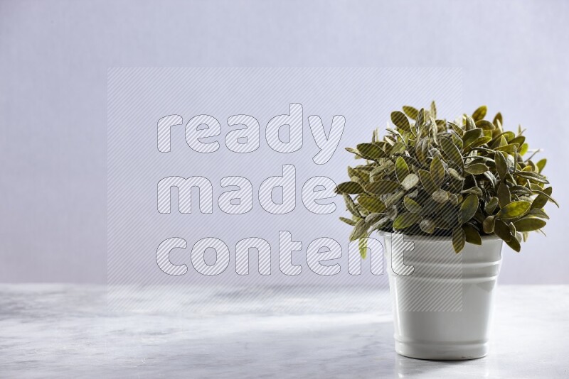 Multiple green artificial plants in white pot on grey marble background