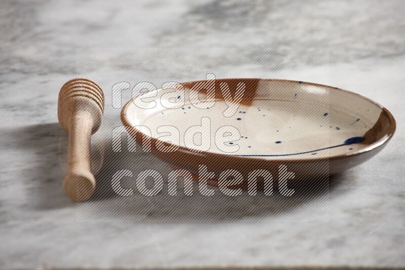 Multicolored pottery plate with wooden honey dipper on the side on grey marble background