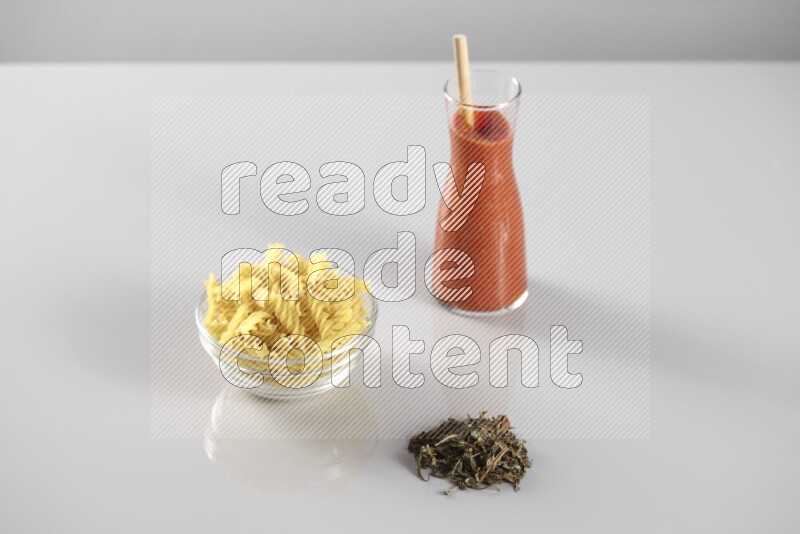 Raw pasta with tomatoe pasta with different ingredients such as cherry tomatoes, basil, garlic, bay laurel, cardamom, white pepper, black pepper, red chilis and wheat stalks on light grey background