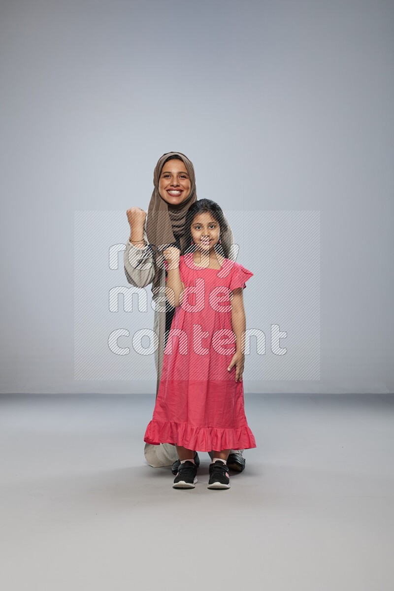 A girl and her mother interacting with the camera on gray background