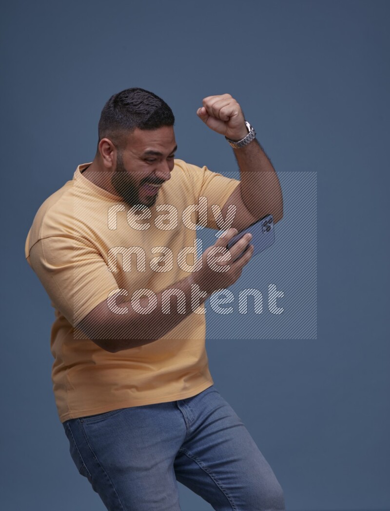 A man Playing Games on Smartphone on Blue Background wearing Orange T-shirt