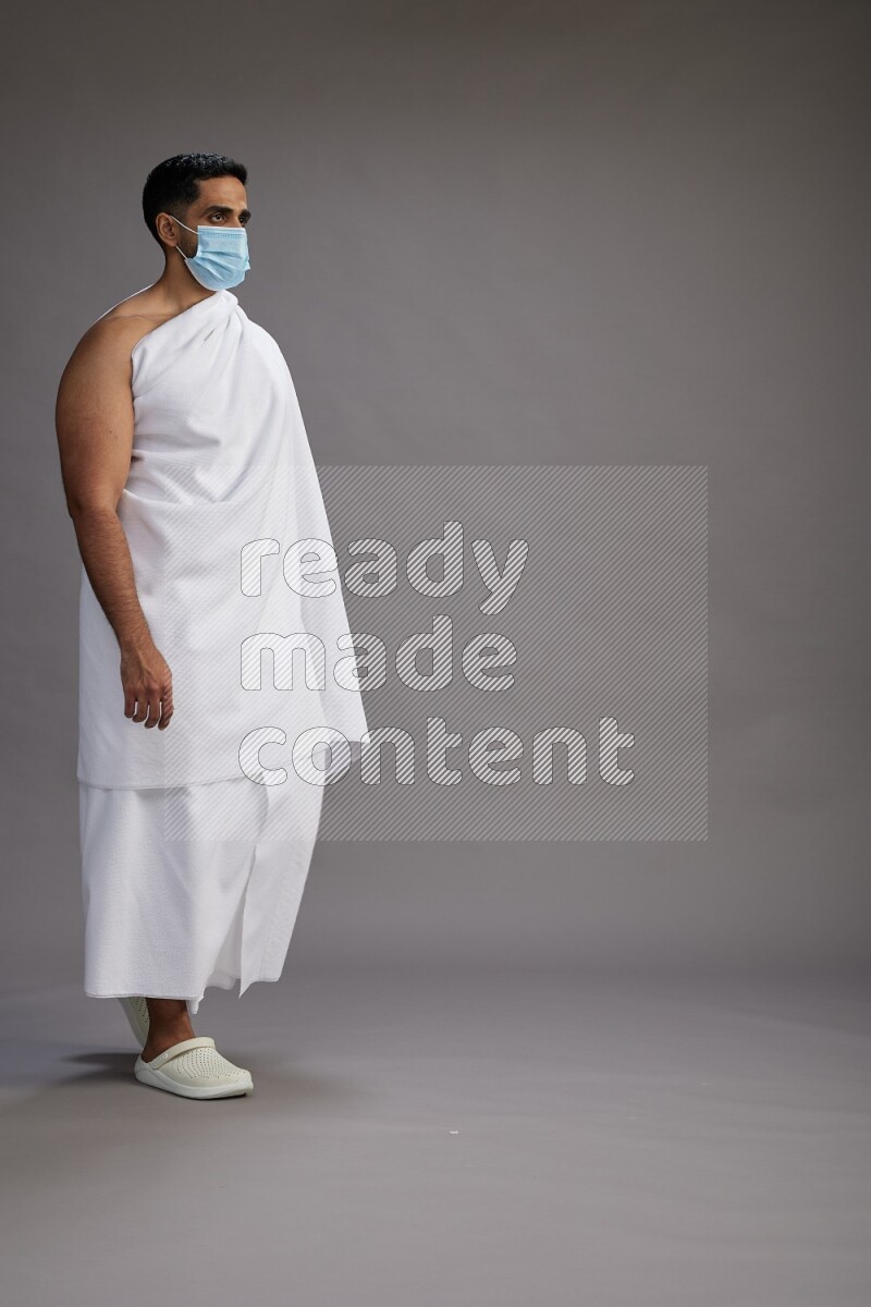 A man wearing Ehram with face mask Standing Interacting with the camera on gray background