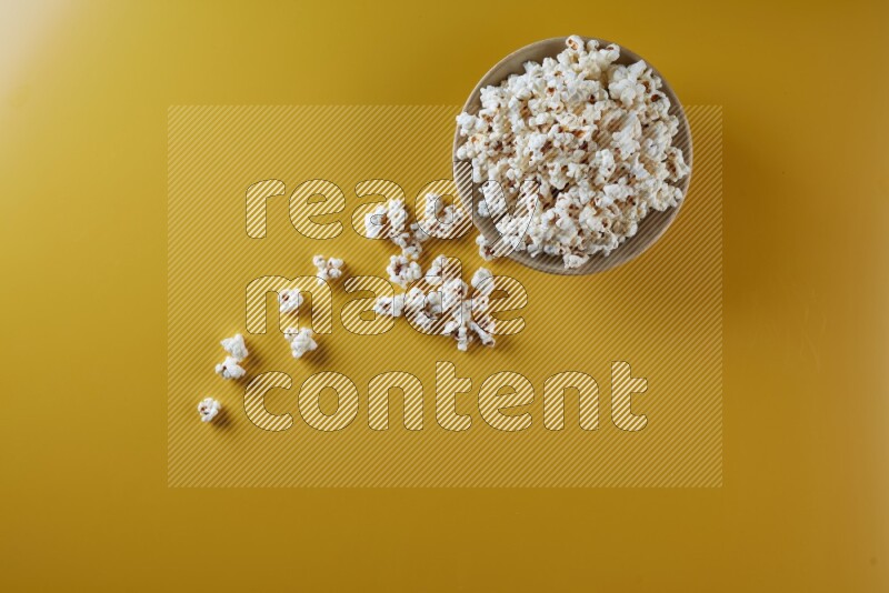 A multicolored ceramic plate full of popcorn with popcorn beside it on a yellow background in different angles