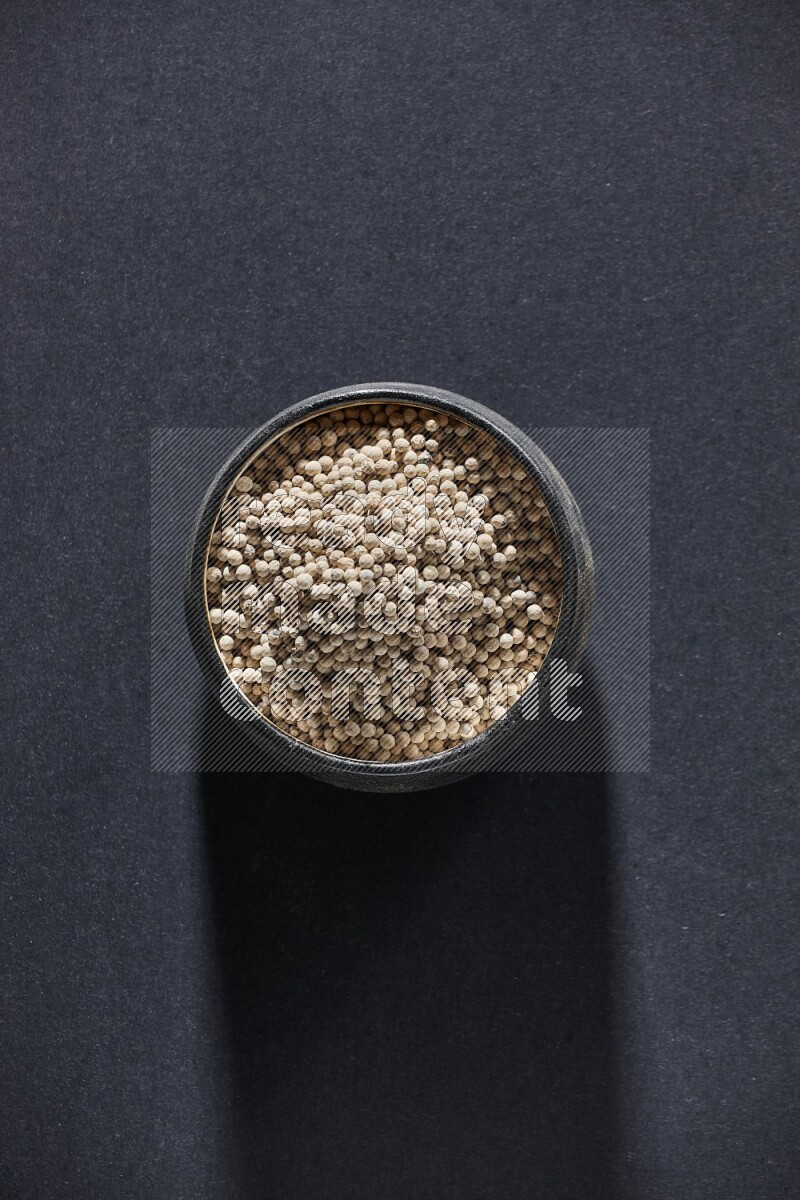 Black pottery bowl full of white pepper on black flooring