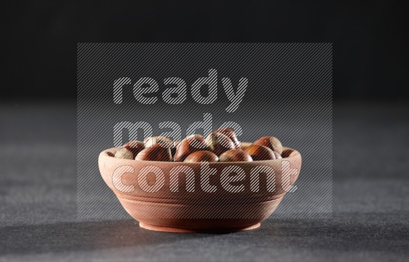 A wooden bowl full of hazelnuts on a black background in different angles