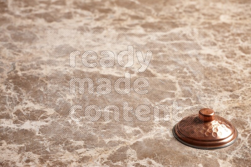 A small copper pot lid on beige marble background