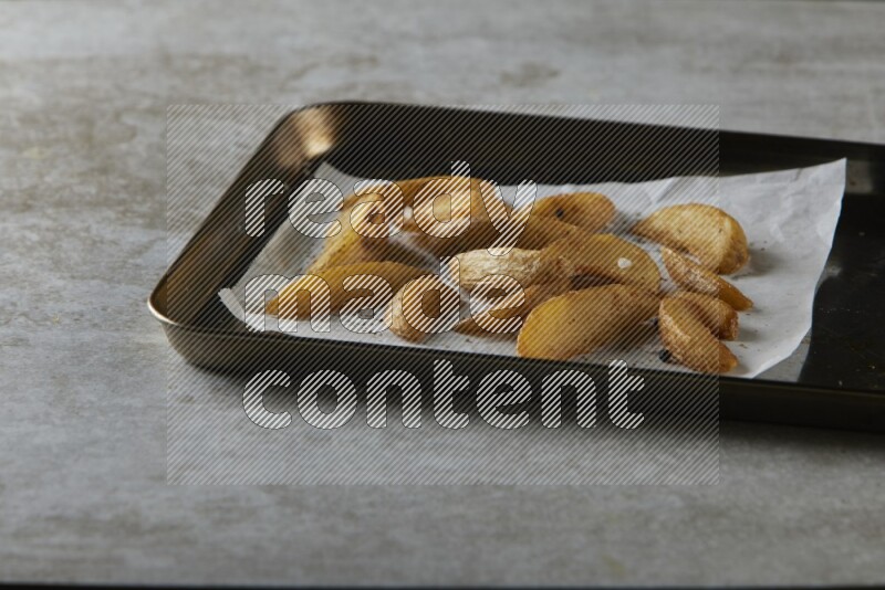 wedges potato on parchment paper in a black stainless steel rectangle tray on grey textured counter top