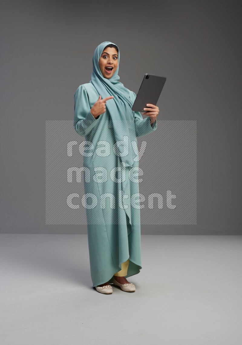 Saudi Woman wearing Abaya standing working on tablet on Gray background