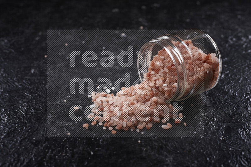 A glass jar full of coarse himalayan salt crystals on black background