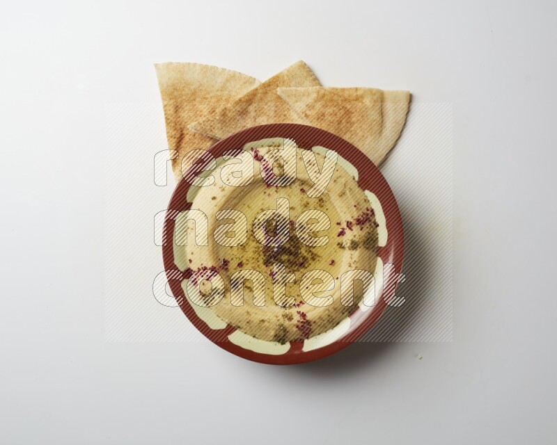Hummus in a traditional plate garnished with zaatar & sumak on a white background