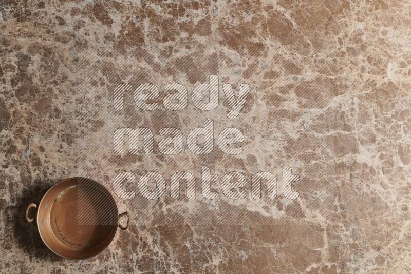 A small copper pan on beige marble background
