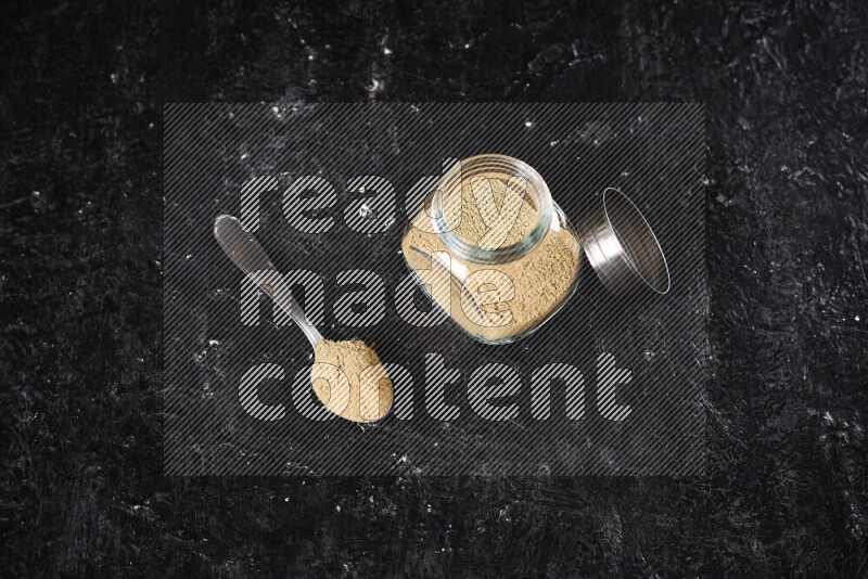 A glass jar full of ground ginger powder on black background