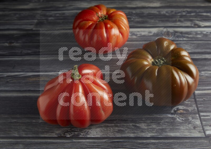45 degree three heirloom tomato on a textured grey wooden background