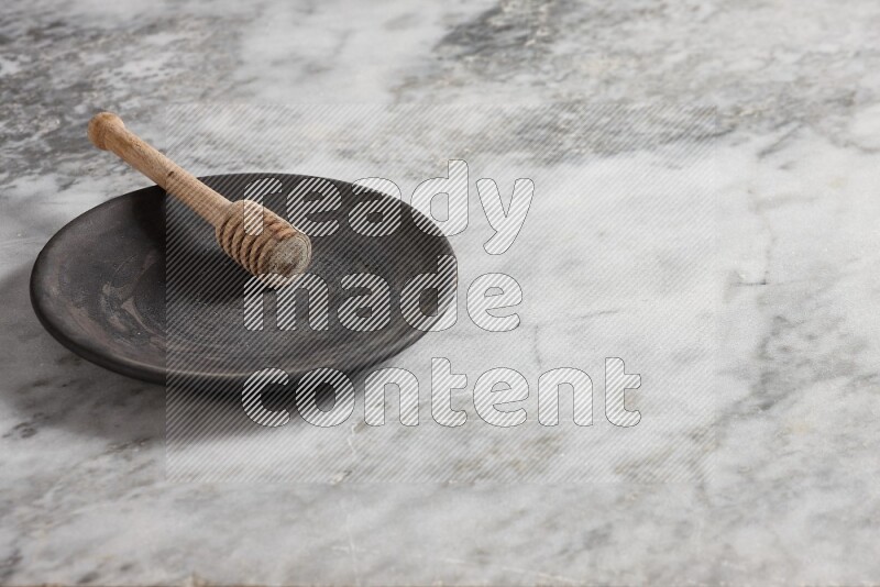 طبق فخاري أسود مع ملعقة عسل خشبية بداخله على خلفية من الرخام الرمادي