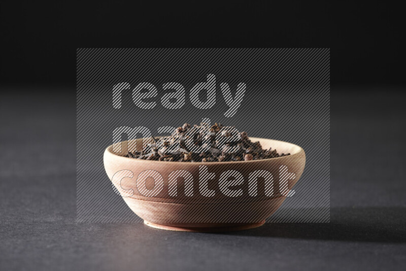 A wooden bowl full of cloves on a black flooring
