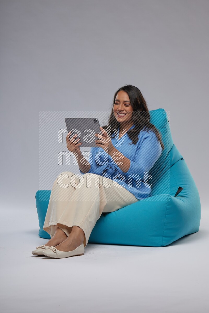 A woman sitting on a blue beanbag and working on tablet