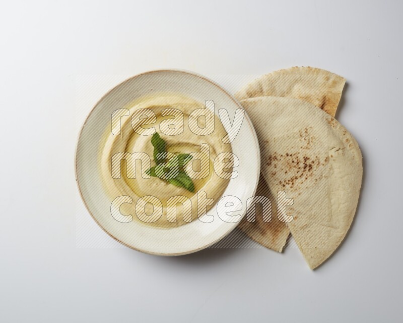 Hummus in a pottry plate garnished with mint  on a white background