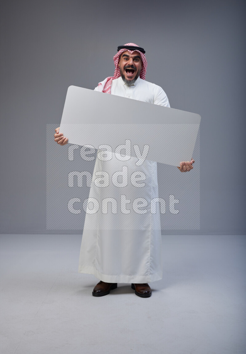 Saudi man Wearing Thob and red Shomag standing holding board on Gray background