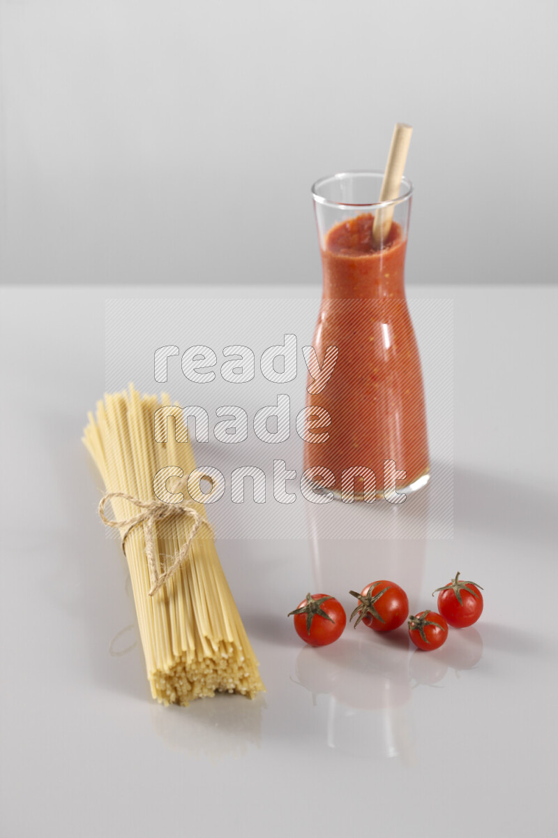 Raw pasta with tomatoe pasta with different ingredients such as cherry tomatoes, basil, garlic, bay laurel, cardamom, white pepper, black pepper, red chilis and wheat stalks on light grey background