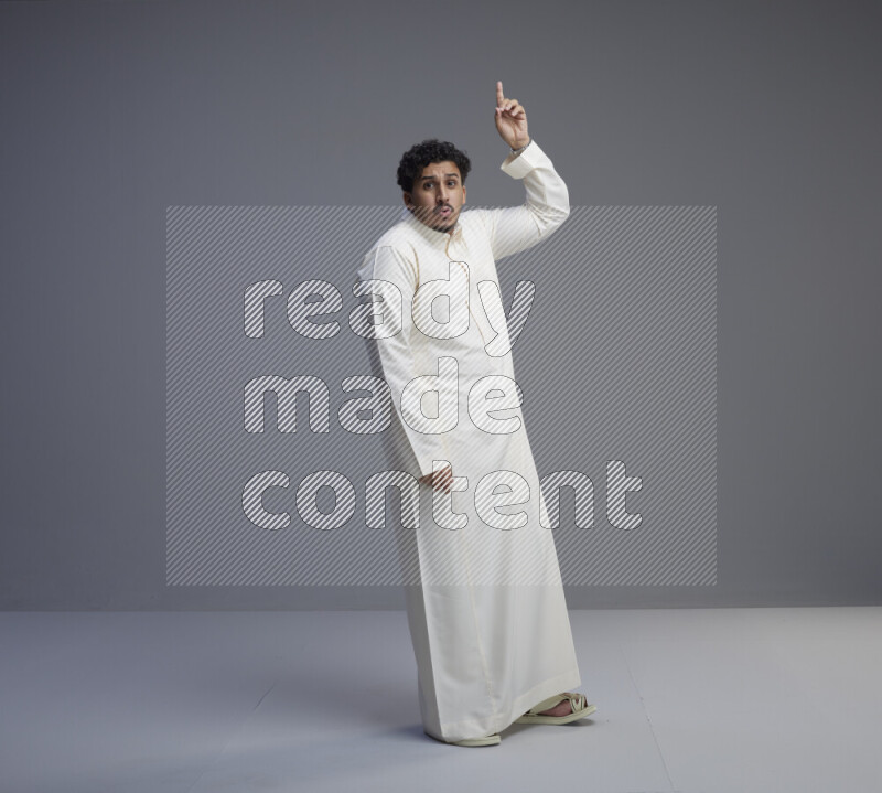A Saudi man standing wearing thob interacting with the camera on gray background