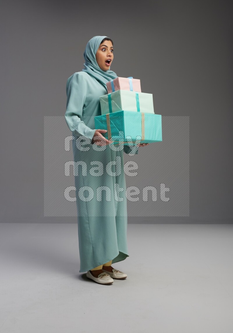Saudi Woman wearing Abaya standing holding gift box on Gray background