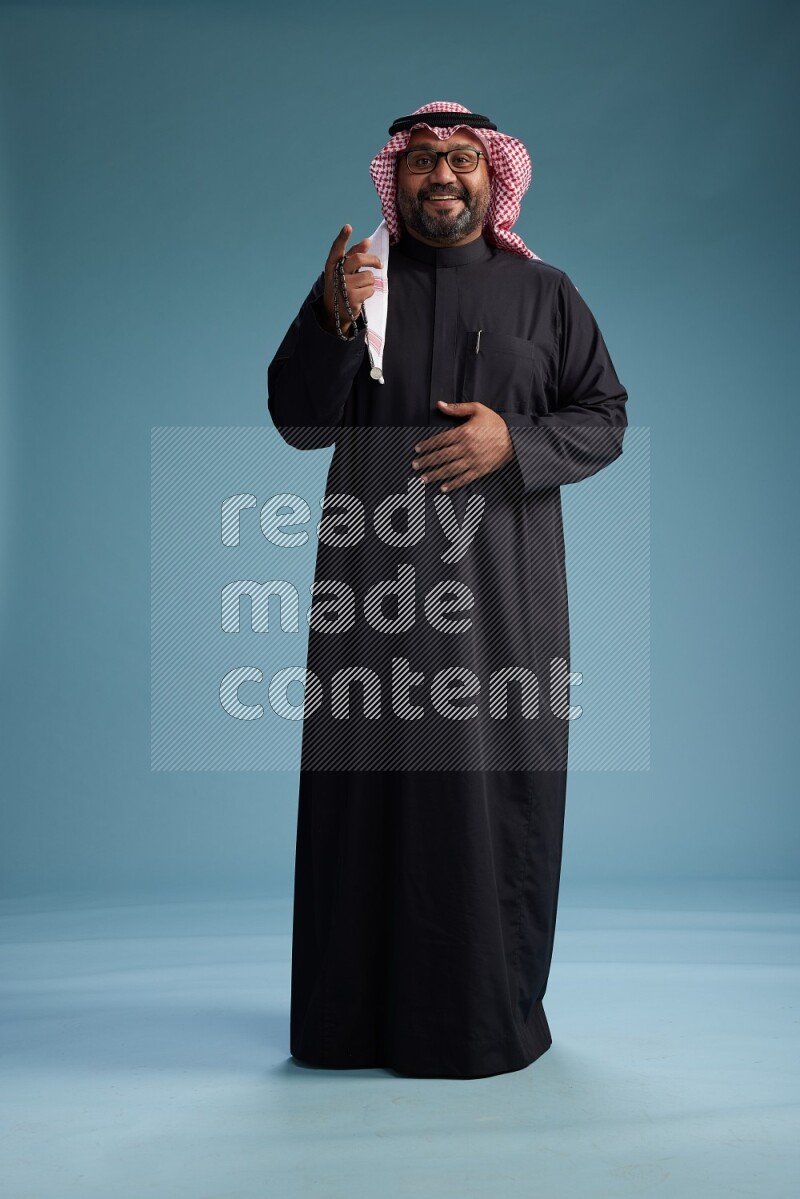 Saudi Man with shimag Standing Interacting with the camera on blue background