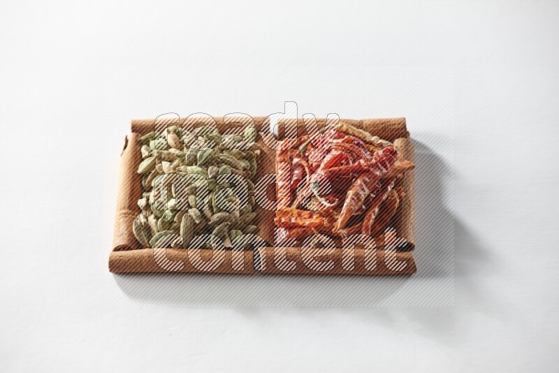 مربعان من أعواد القرفة ممتلئان بحبوب الهيل والفلفل الحار المجفف علي خلفية بيضاء