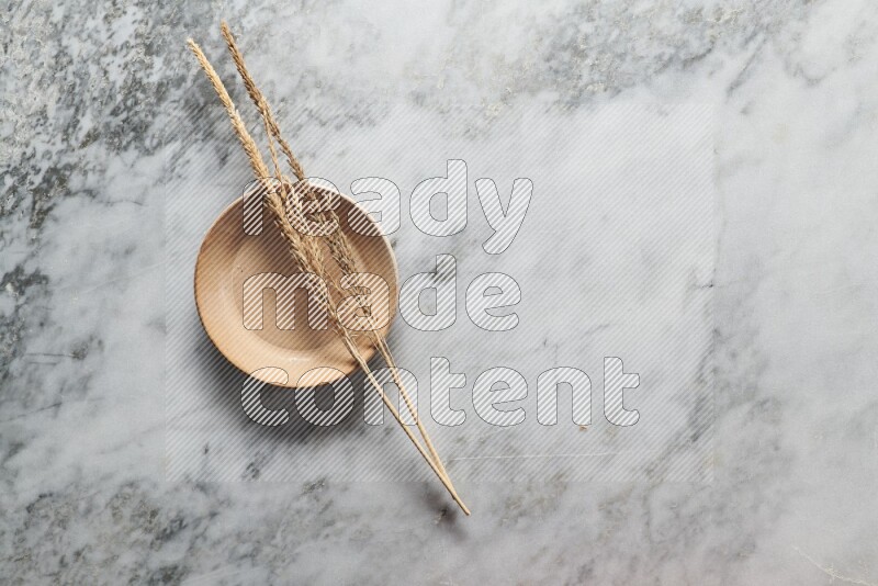 Wheat stalks on beige pottery plate on grey marble background