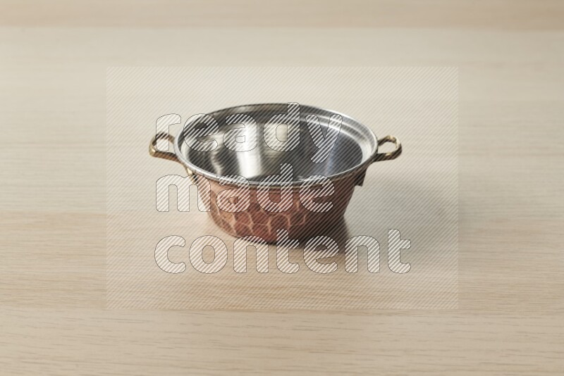 A small copper pot on light wooden background