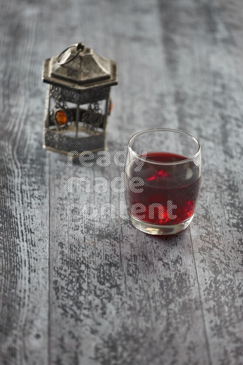 A silver lantern with different drinks, dates, nuts, prayer beads and quran on grey wooden background