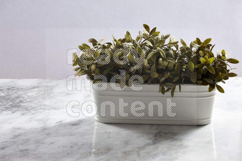 Multiple green artificial plants in white pot on grey marble background