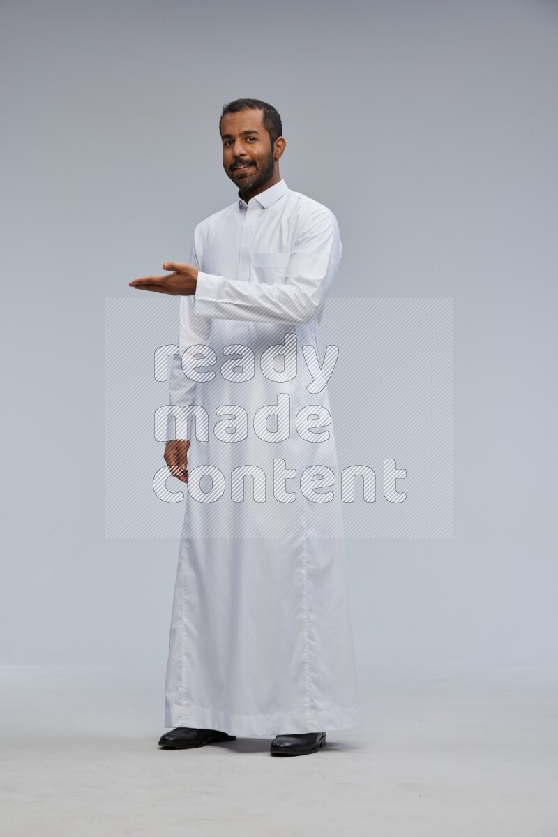 Saudi man Wearing Thob standing interacting with the camera on Gray background