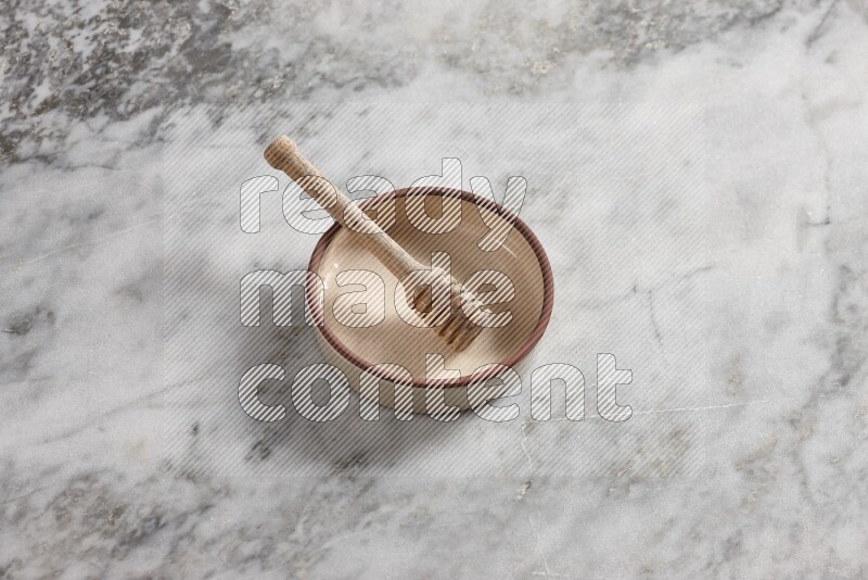 Beige Pottery oven bowl with wooden honey handle on the side with grey marble flooring, 65 degree angle