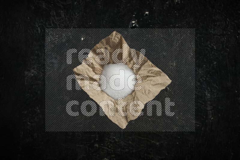 A crumpled piece of paper full of white salt on black background