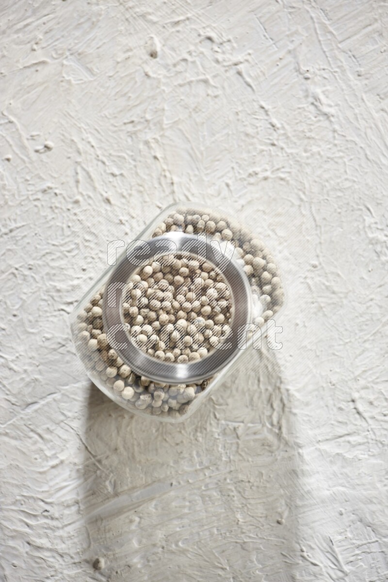 Herbal Glass jar full of white pepper beads on textured white flooring