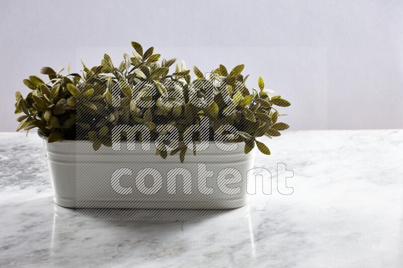 Multiple green artificial plants in white pot on grey marble background