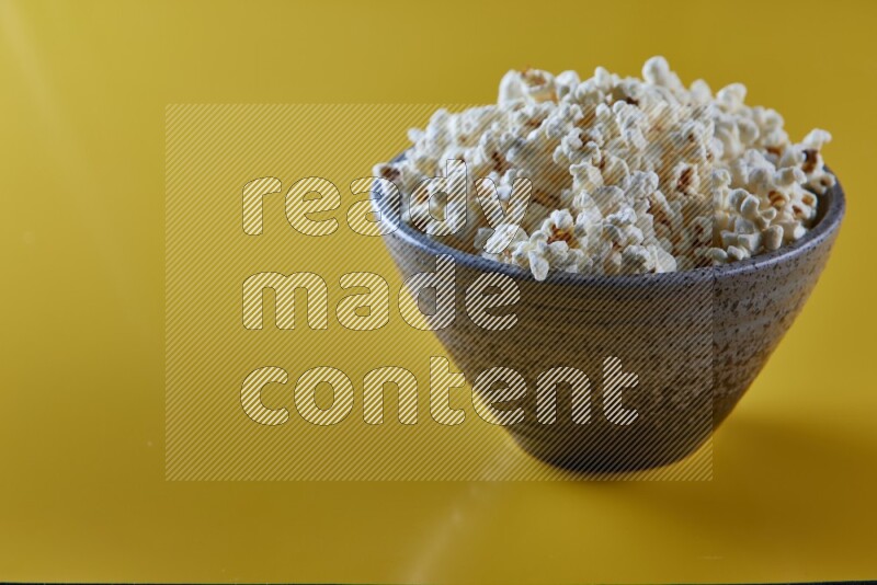 A multicolored pottery bowl full of popcorn on a yellow background in different angles