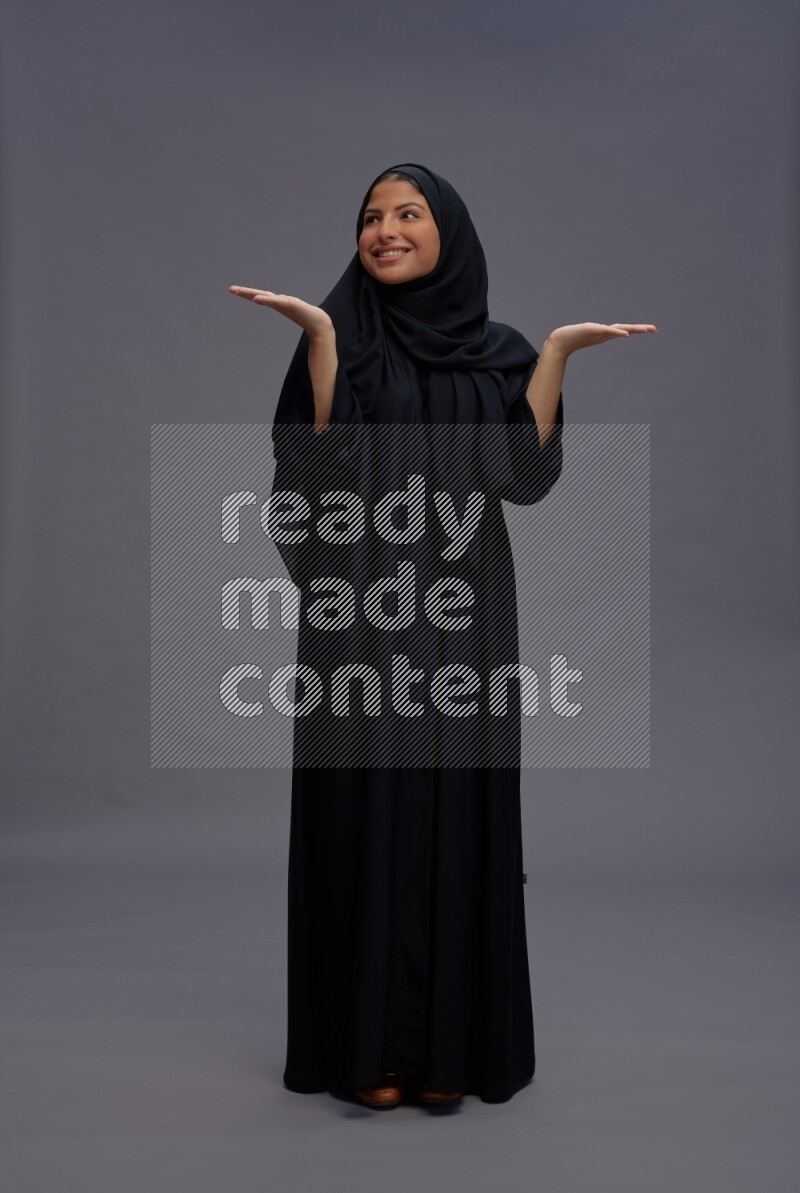 Saudi woman wearing Abaya standing interacting with the camera on gray background