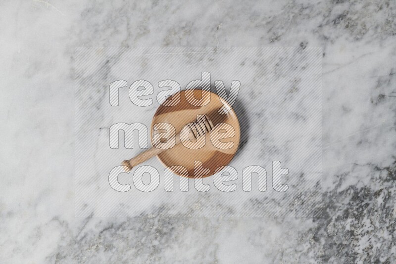 Multicolored pottery plate with wooden honey dipper in it on grey marble background
