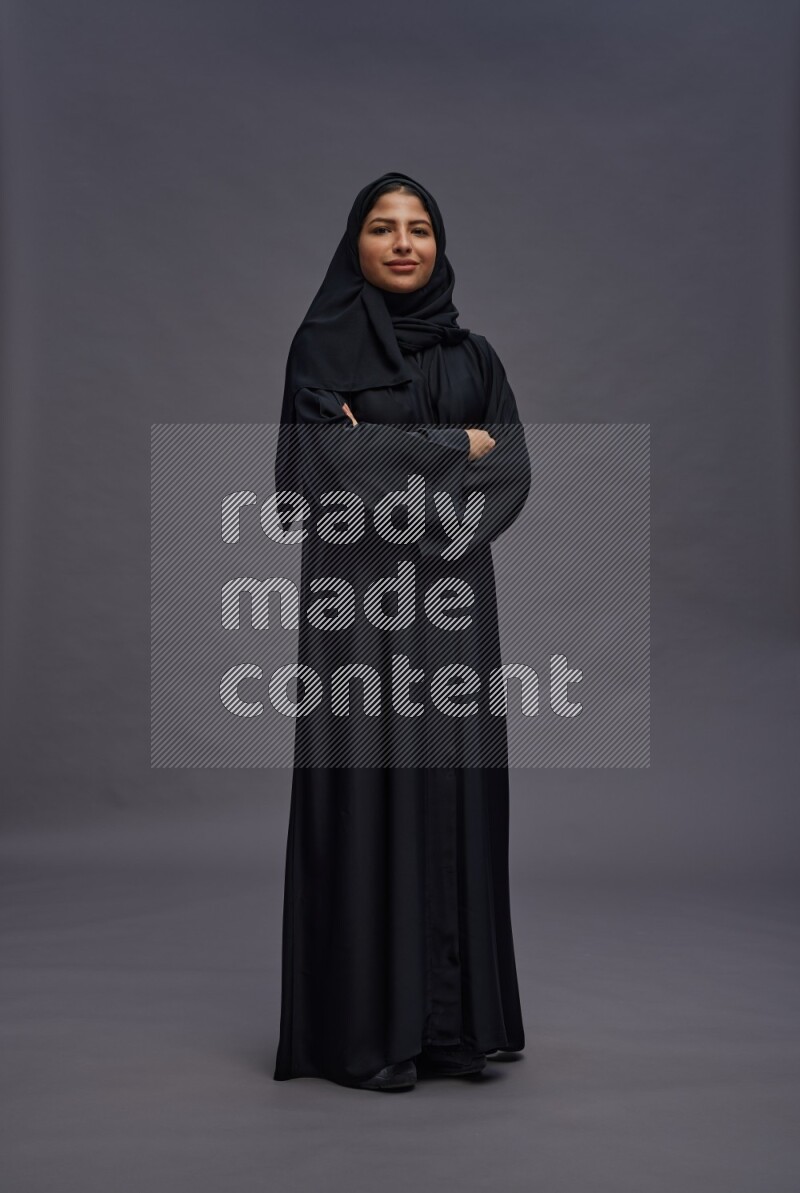 Saudi woman wearing Abaya standing with crossed arms on gray background