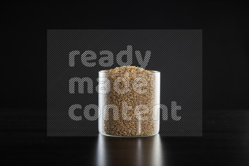 Hulled wheat in a glass jar on black background