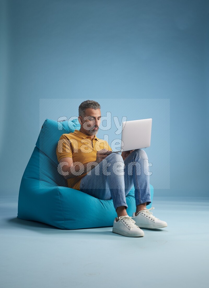 A man sitting on a blue beanbag and working on laptop
