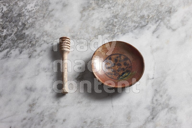 Decorative pottery plate with wooden honey dipper on the side on grey marble background
