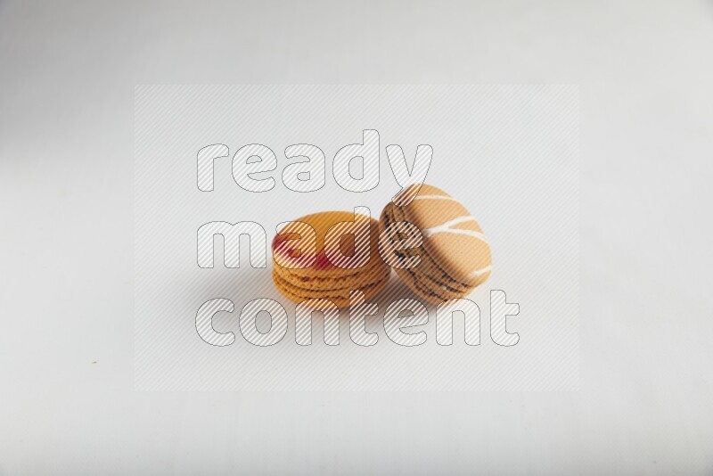 45º Shot of of two assorted Brown Irish Cream, and Orange Exotic macarons on white background