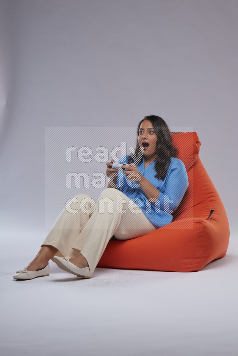 A woman sitting on an orange beanbag and gaming with joystick