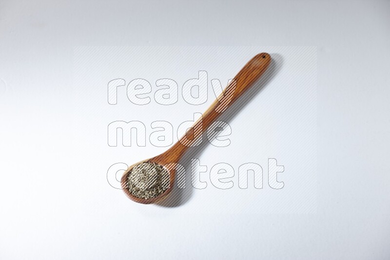 A wooden ladle full of cumin seeds on a white flooring